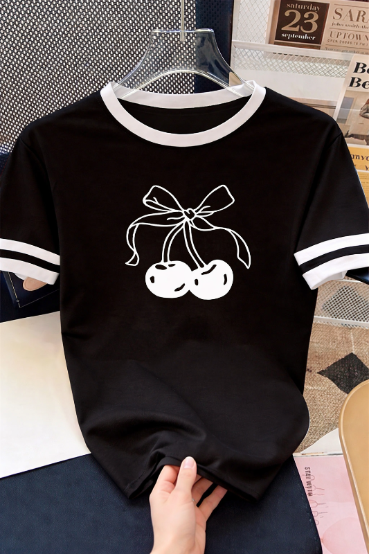 Black t-shirt with white cherry and bow design held by a hand on a surface.