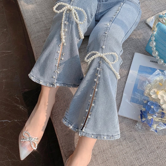 Light blue jeans with pearl details worn by a person, sitting on a textured surface.