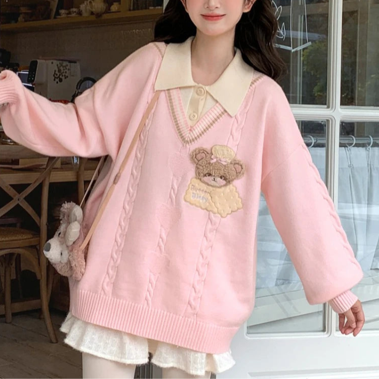 Woman wearing a pink sweater with a teddy bear design indoors.