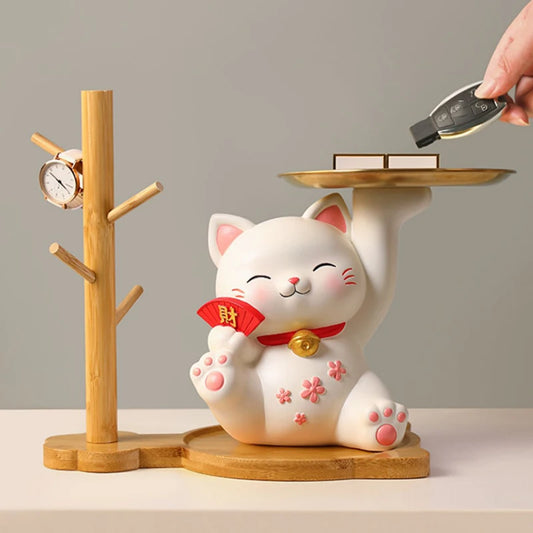 White cat-shaped figurine with a red ribbon on a wooden stand, holding a small tray.