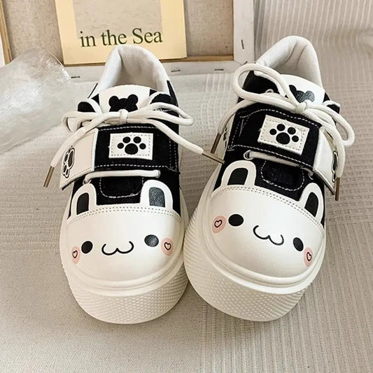 Pair of cute neko white sneakers with black accents and cute face designs on a neutral background