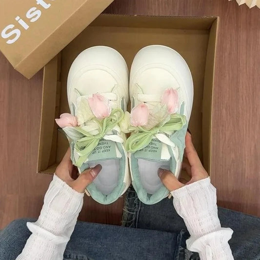 White sneakers with floral decorations held by a person in front of an open box.