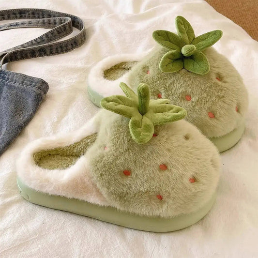 green strawberry slippers worn indoors on a white blanket.
