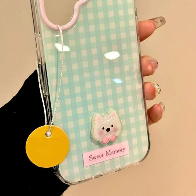 Phone case with checkered design, pink dog design, and 'Sweet Memory' tag held by a hand.