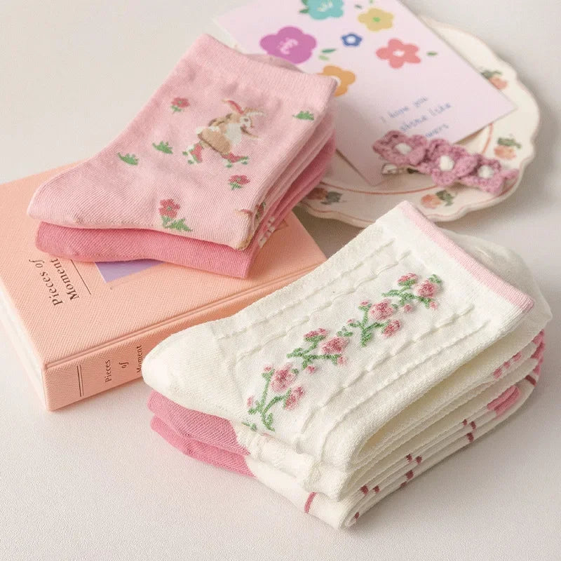 Stack of pink and white socks on a light surface with books and decorative items.