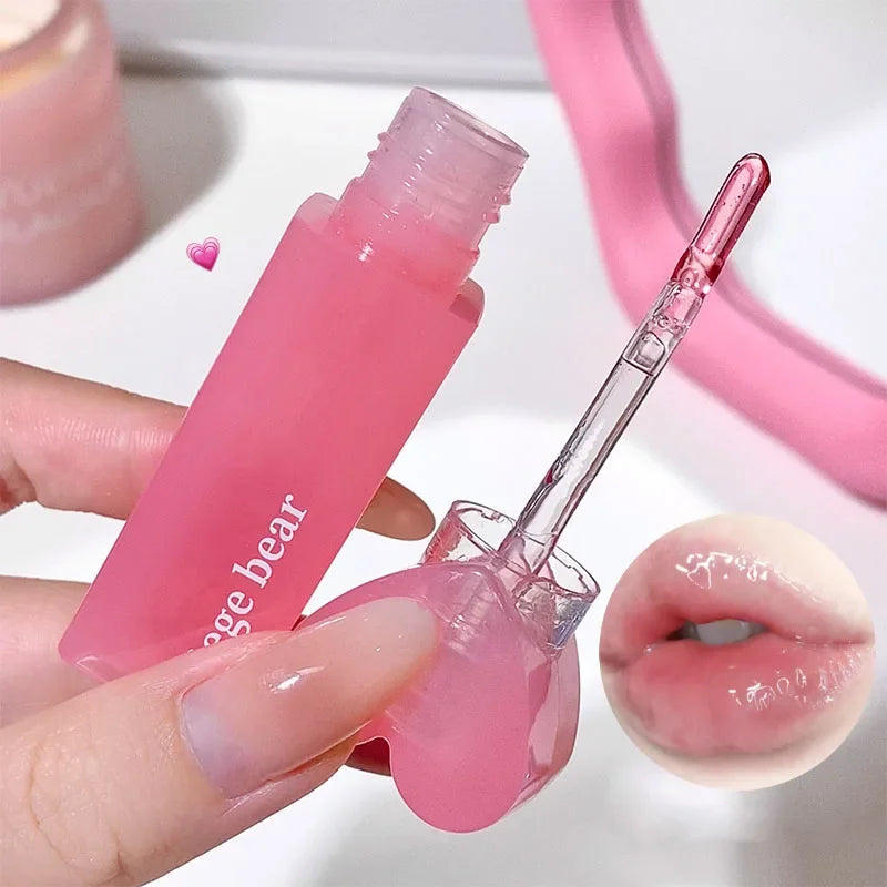 Pink lip gloss with applicator held by a hand, close-up view.