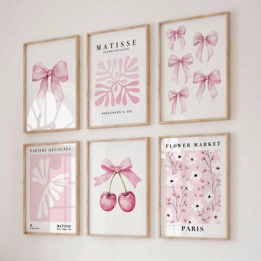 Six framed art prints arranged in a 2x3 grid on a light wall. The prints feature pink watercolor motifs including bows, cherry blossoms, flowers, and abstract shapes, with some prints displaying the text 'MATISSE', 'PARIS', and 'PARISERS DÉCOUPES'.