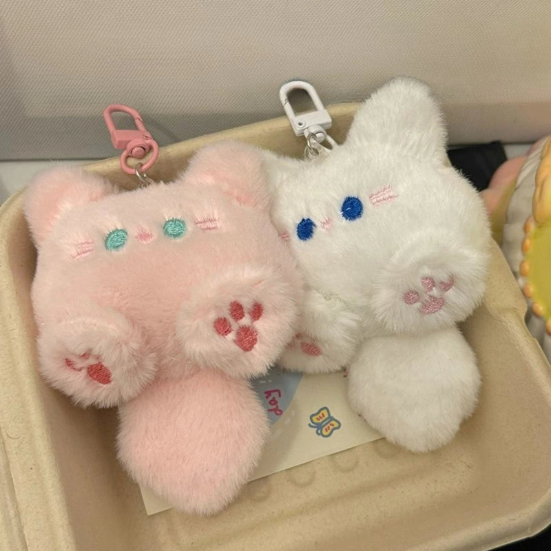 Two fluffy cat-shaped keychains, one pink and one white, on a beige surface.
