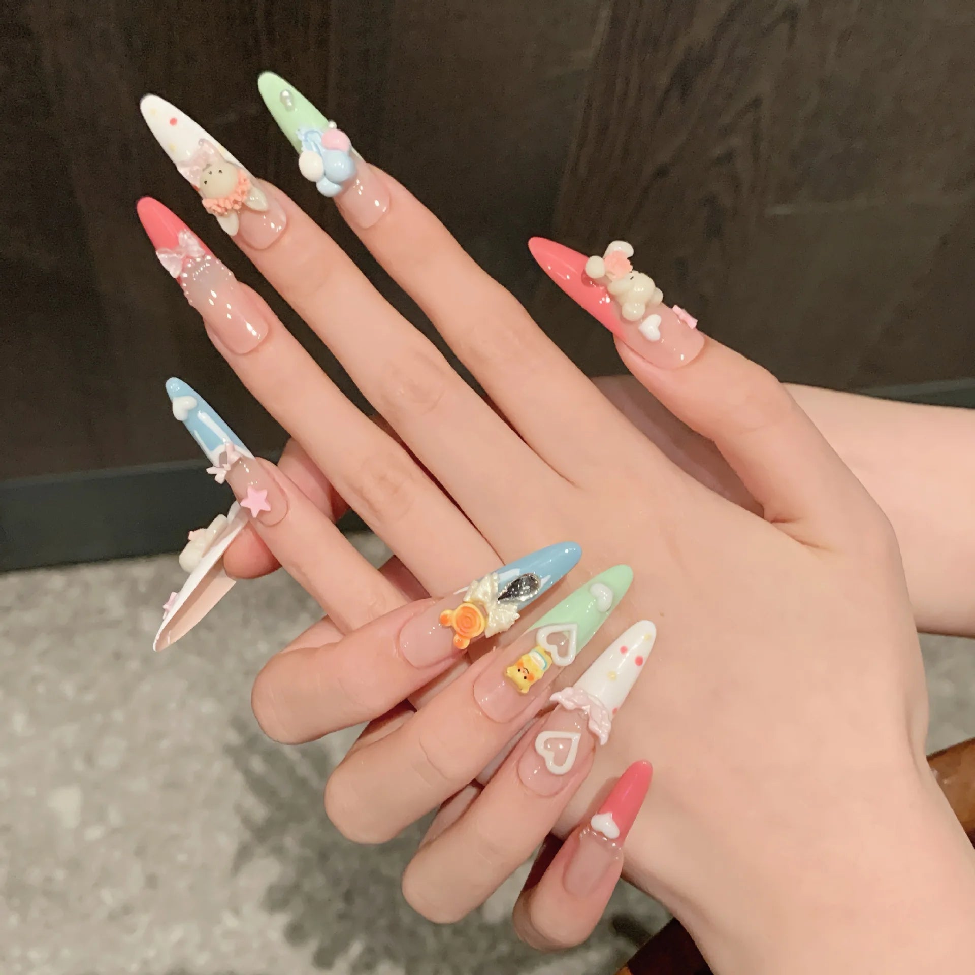 Hand with intricately designed nails featuring various kawaii shapes and colors.