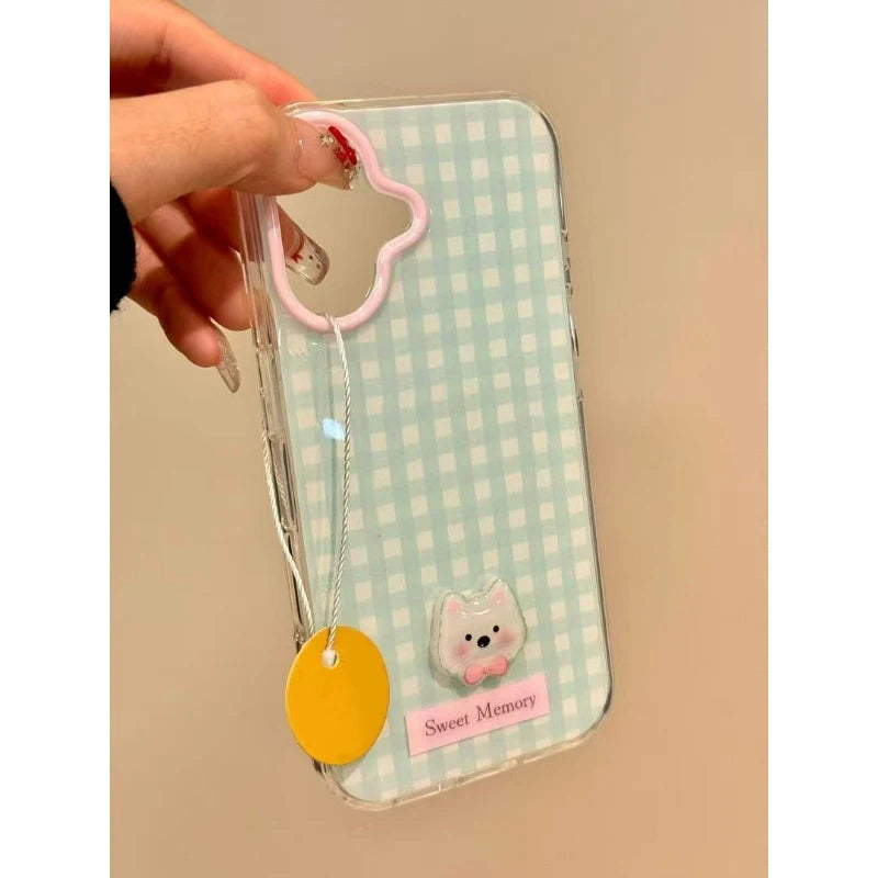 Phone case with a checkered pattern, pink dog charm, and yellow tag held by a hand on a beige background.