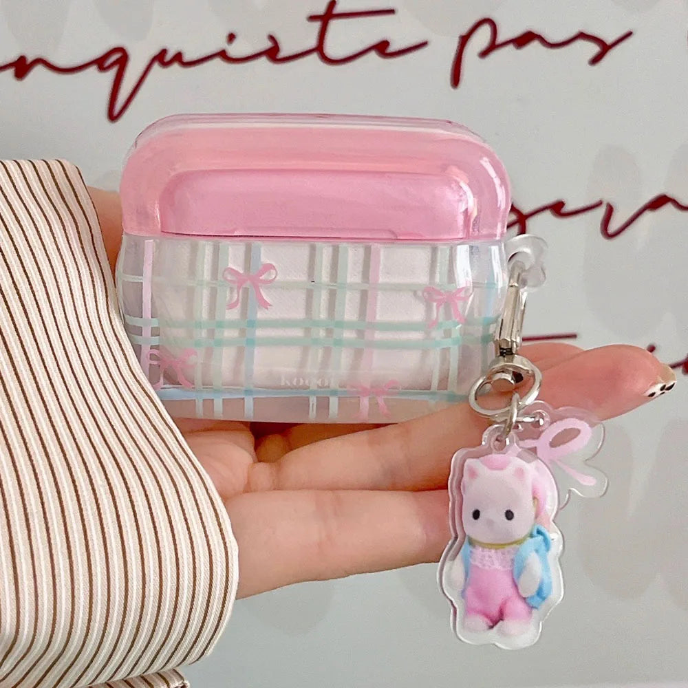 Small pink and clear kawaii airpods case with a keychain charm held by a hand against a blurred background.