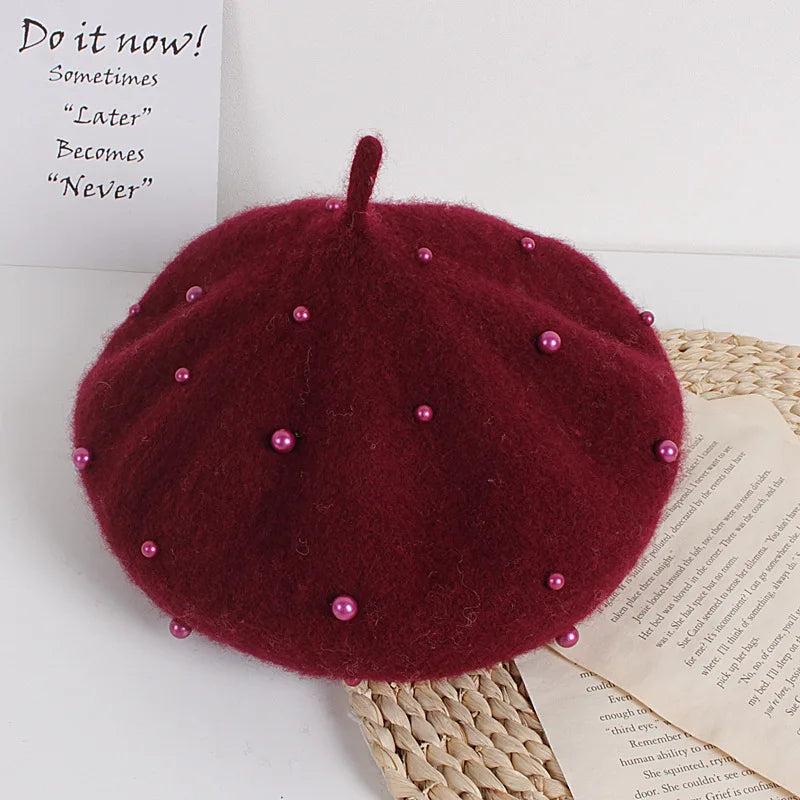 Dark Red beret with pink beads on a white surface with text and paper.