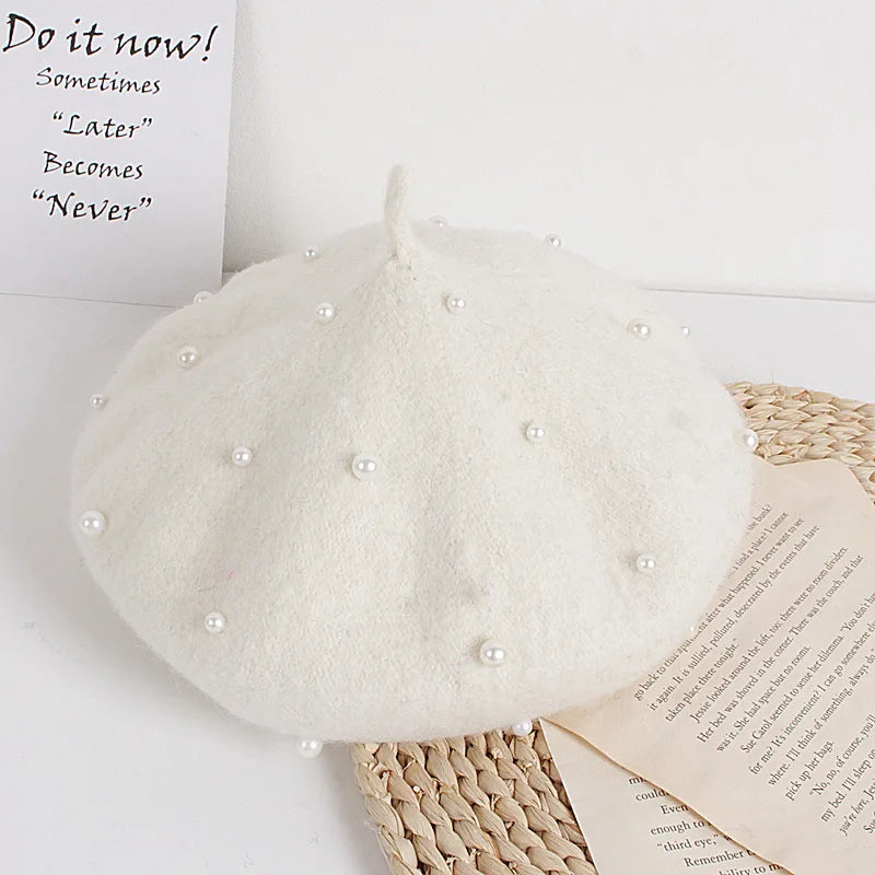 White beret with pearl embellishments on a white surface with text and paper.