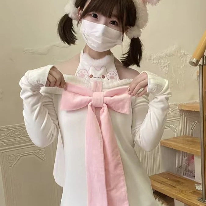 Person wearing a white outfit with a pink bow and fluffy ears hat in a room with wooden stairs.