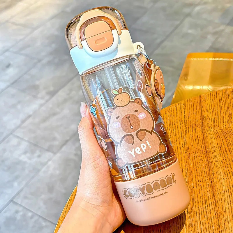 Clear water bottle with capybara design held by a hand on a wooden surface.