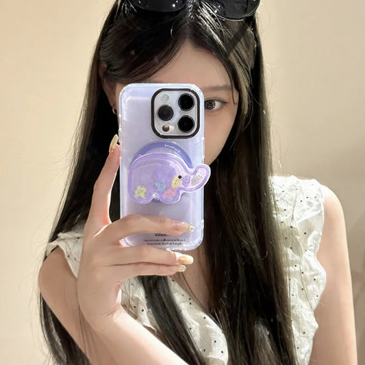 a woman holding a phone with the kawaii cute elephant quicksand phone grip , this is in the color purple with colorful elephant faces inside