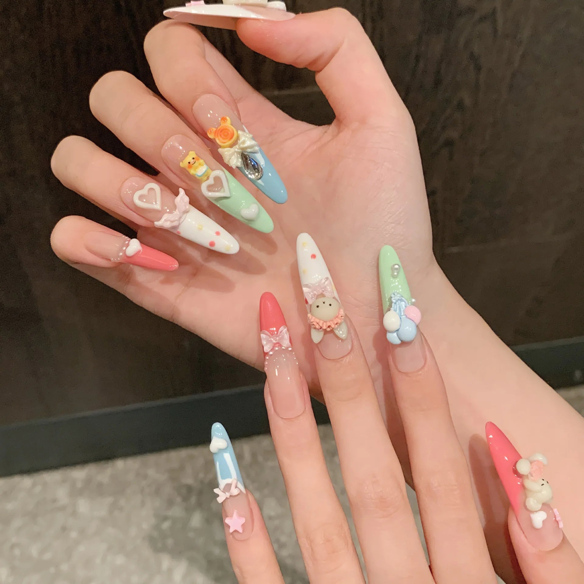 Hand with pastel-colored nail art featuring cute designs on a dark background