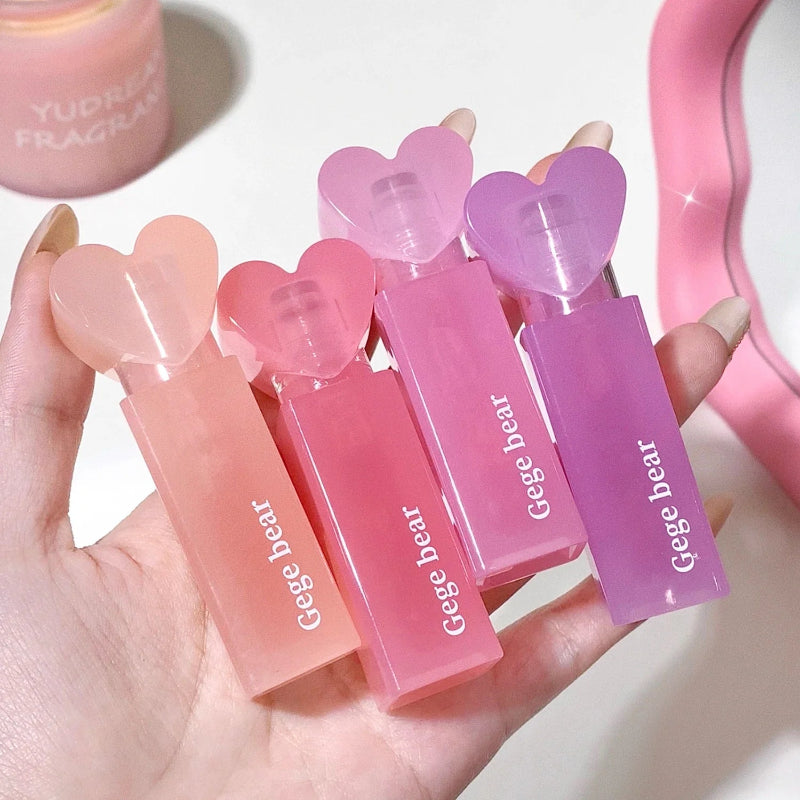 Hand holding four pink lip glosses with heart-shaped caps, branded 'Geege bear', on a light background.
