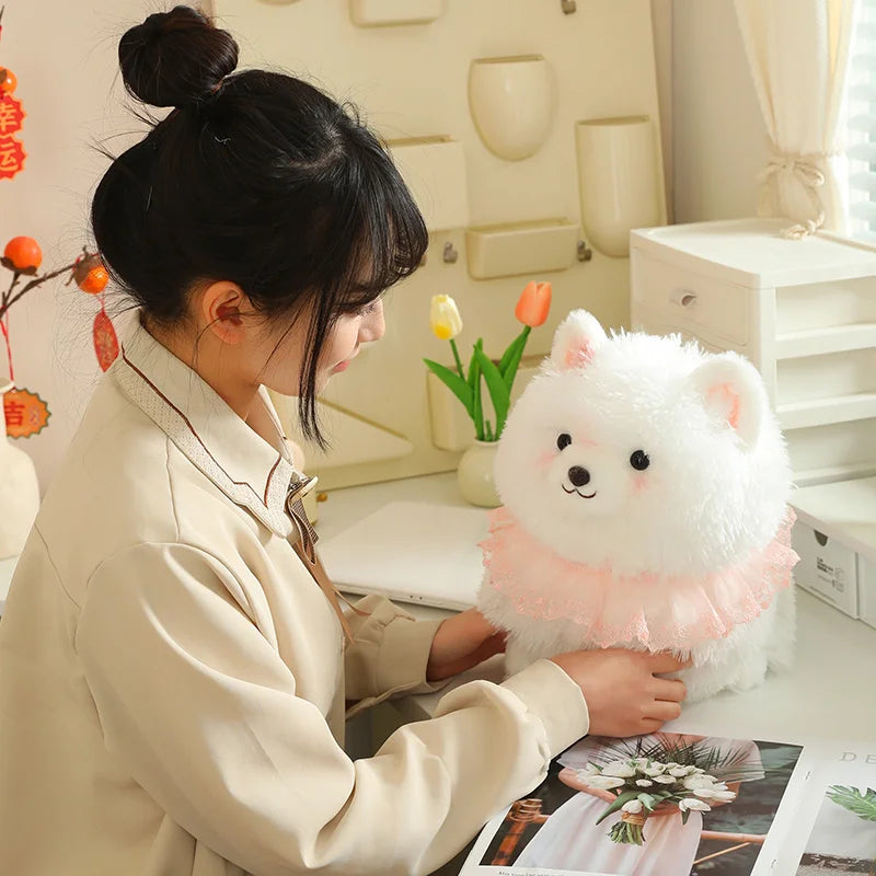 Person playing with a white pomeranian plush toy on a desk.