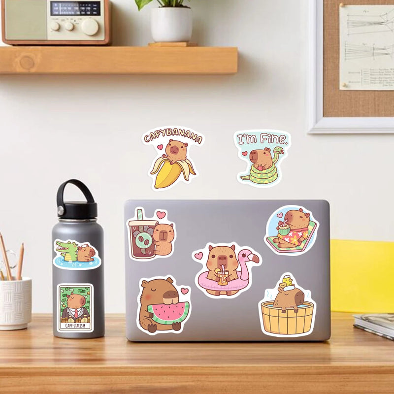 Laptop with various kawaii capybara-themed stickers on a desk, with a water bottle and plant in the background.