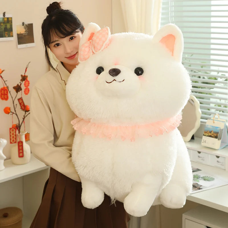 Person holding a large fluffy white pomeranian plush toy with pink accents in a room.
