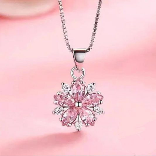 Sakura Cherry Blossom Necklace the hot pink version is displayed on a pastel pink silky background hanging from a sterling silver chain