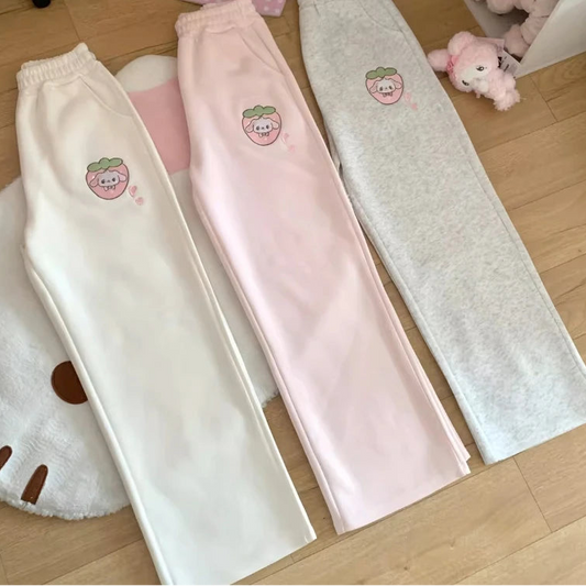 Three pairs of kawaii pants in white, pink, and gray with embroidered designs on a wooden floor.