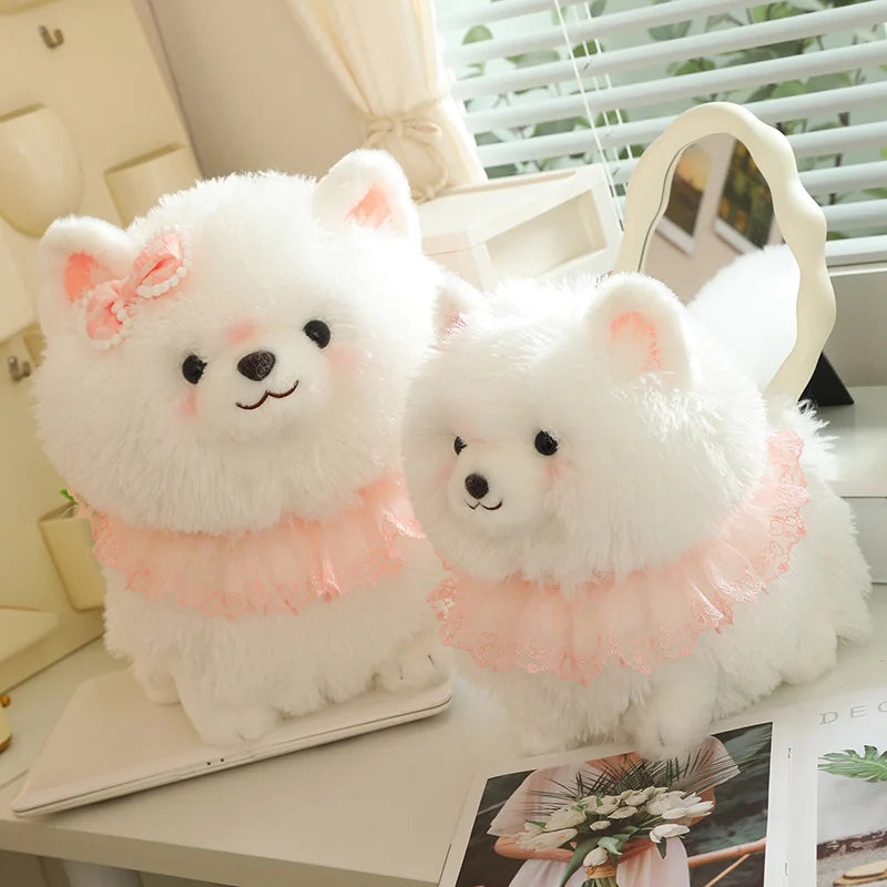 Two fluffy white pomeranian plush toys with pink collars on a table.