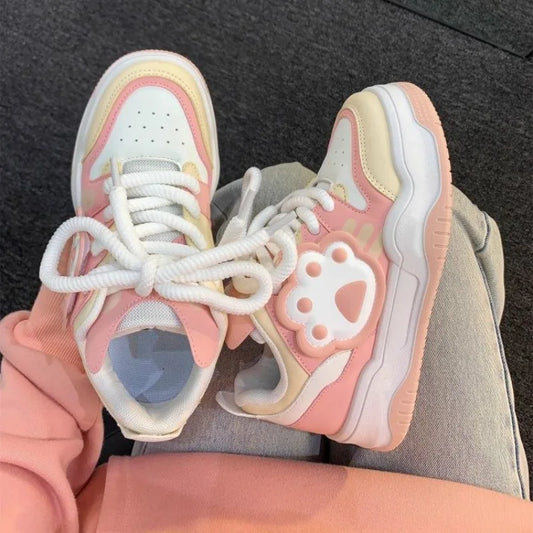 Pair of pink and white sneakers with a cat paw design on a dark background