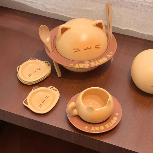 A cute cat-themed dinnerware set on a dark wooden table, featuring a cat-shaped bowl with chopsticks, matching plates, a small cup, and a spherical container, all in a warm pastel peach and orange color scheme.