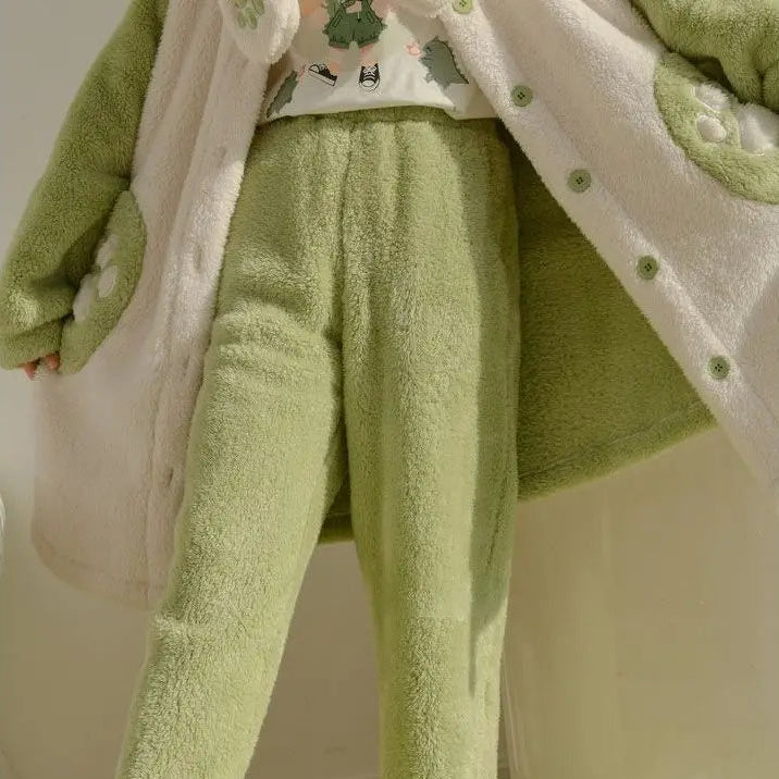 A person wearing a plush fleece pajama set in light green, including matching pants and a button-front cardigan with a white sherpa lining and small printed motifs.