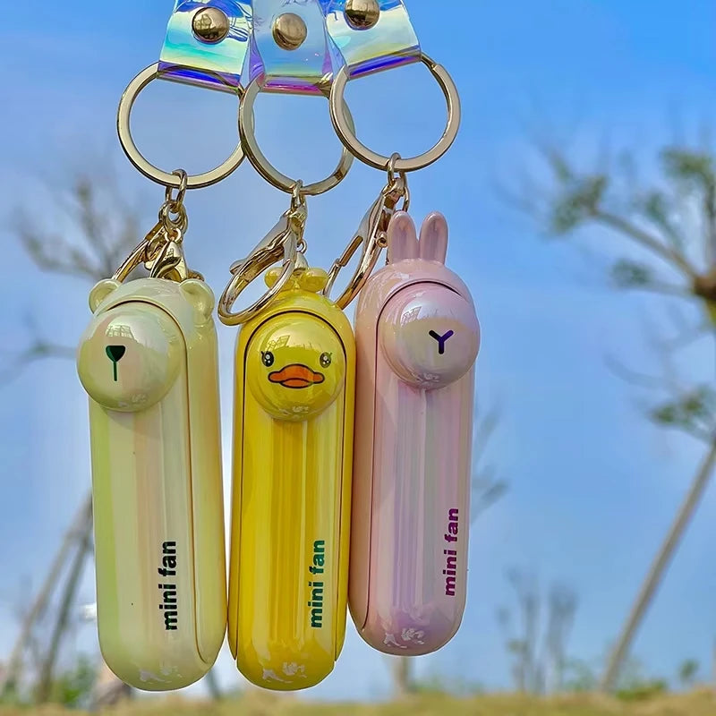 Three mini fans with animal designs and 'mini fan' text on a blurred natural background