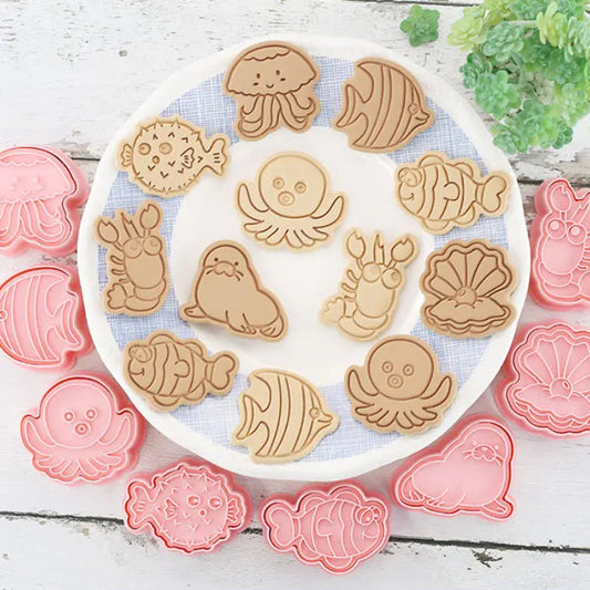 Set of sea creatures -shaped cookie cutters on a white plate with pink and red cutters around.