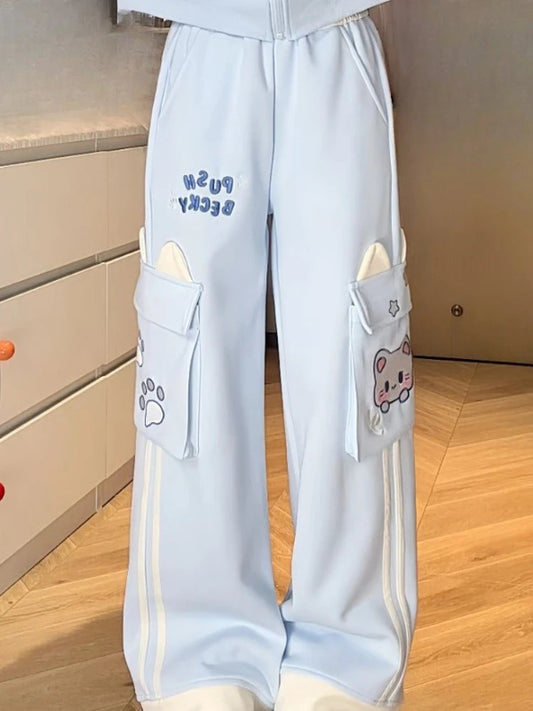 Light blue pants with kawaii cat designs on a wooden floor.