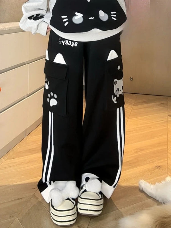 Person wearing black cat-themed pants with white paw prints and stripes indoors.