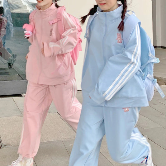 Two children in pink and blue tracksuits standing on a sidewalk.