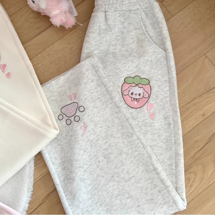 Grey sweatpants with a kawaii design on a wooden floor.