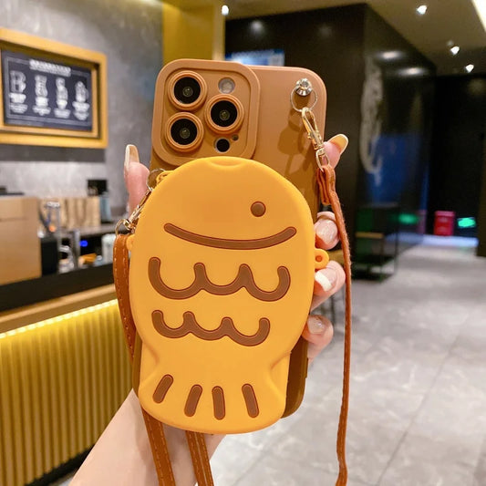 Phone case with cartoon Taiyaki held in a hand, blurred background of a cafe.