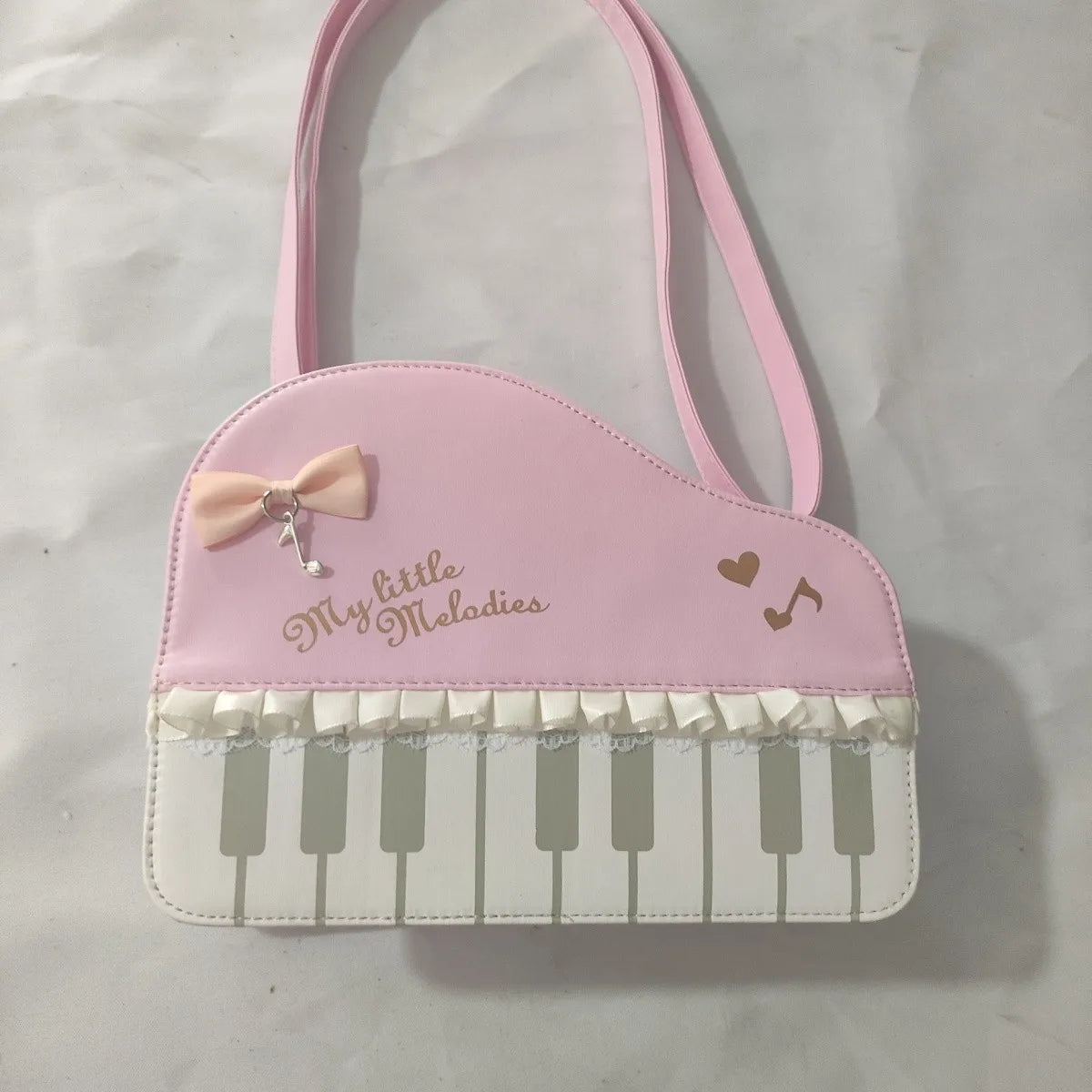 Pink piano-shaped bag with keyboard design and 'My Little Melodies' text on a white background