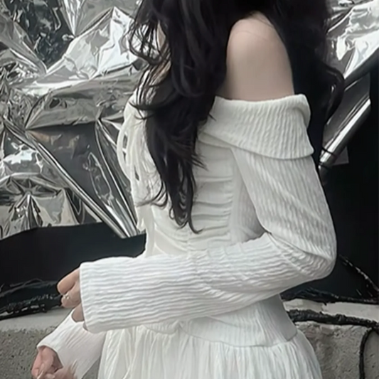 Person wearing a white off-shoulder sweater and skirt against a reflective metallic background.