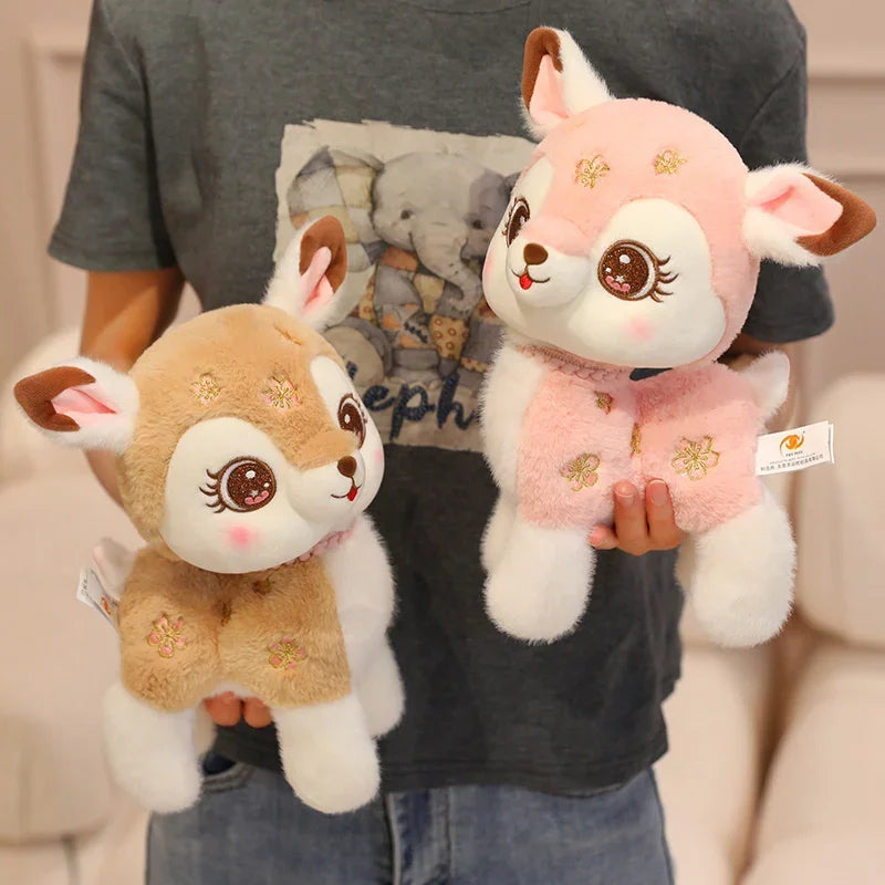 Two plush deer toys held by a person, one pink and one brown, with visible brand tags.