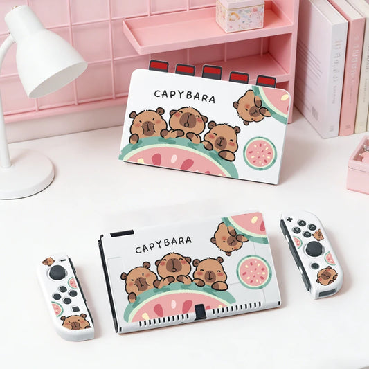 kawaii capybara watermelon switch case, this is the white version with three capybaras holding onto a watermelon while displaying different happy expressions on their faces,it is also showing a white dockcase with the same design holding game cards. this is shown on a white desk.