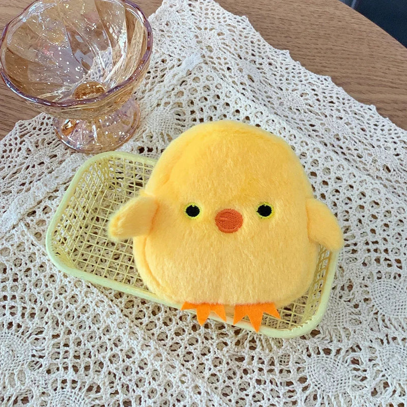 kawaii yellow plush chick coin purse on a textured white surface with a glass bowl in the background.