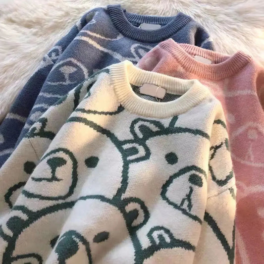 Three sweaters in blue, white, and pink with bear patterns on a fluffy white surface.