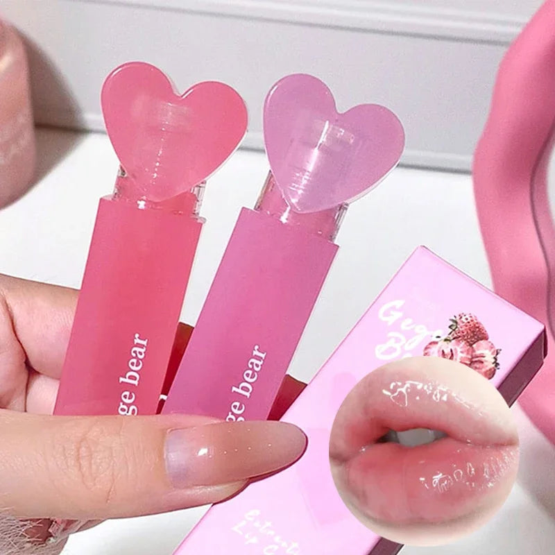 Pink lip gloss with heart-shaped cap held by a hand, close-up of lips with gloss applied.
