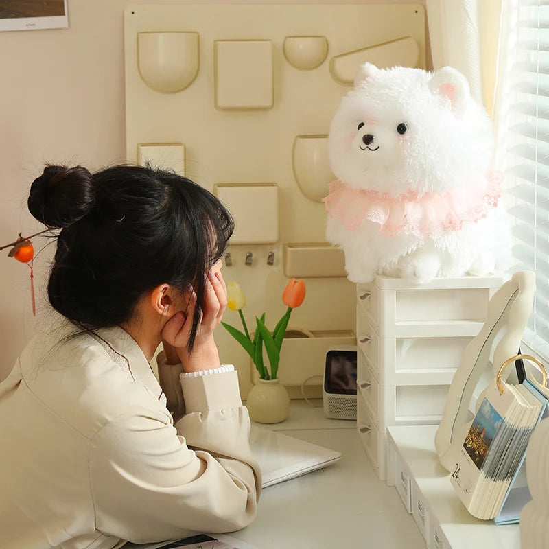 Woman sitting at a desk admiring a fluffy white pomeranian plush toy.