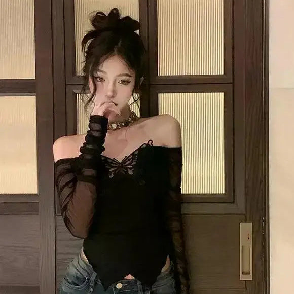 Person wearing a black off-shoulder top and ripped jeans standing in front of a wooden door.