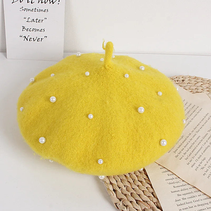 Yellow beret with pearl embellishments on a white surface with a book underneath.