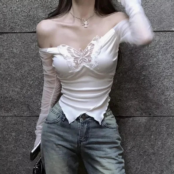 Person wearing a white lace top and light blue jeans against a gray wall.