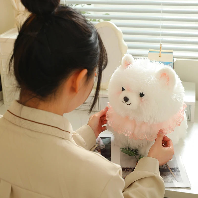 Person playing with a fluffy white pomeranian plush toy that is sitting on a desk.